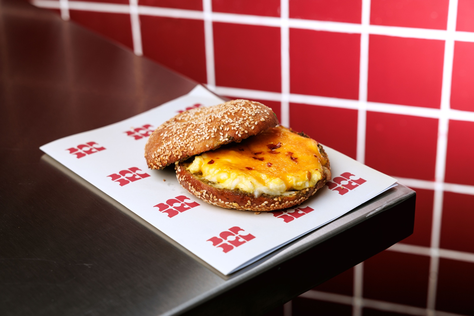 Grilled Cheese Bagel — basil pesto, scramble eggs, cheddar, mozzarella, sour dough sesame bagel